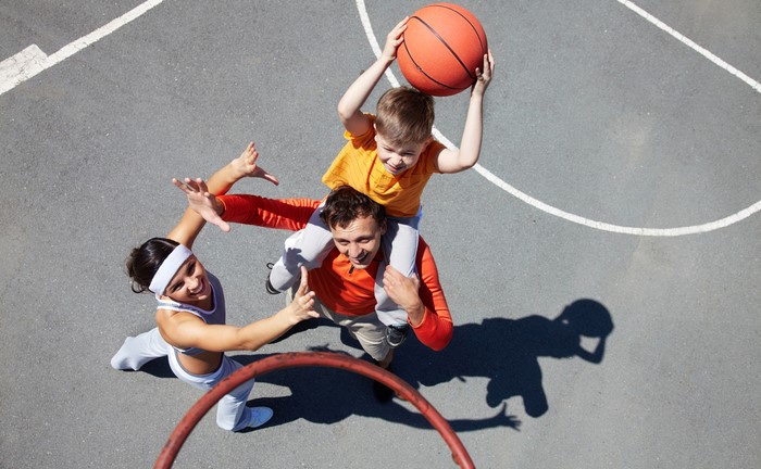 Family playing basketball with son on father’s shoulders holding the ball