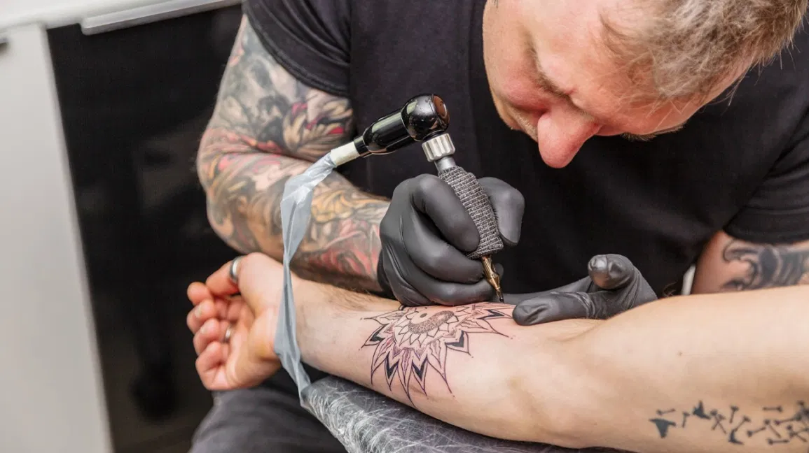Tattoo master puts tattoo in form of flower on arm 1296x728 header