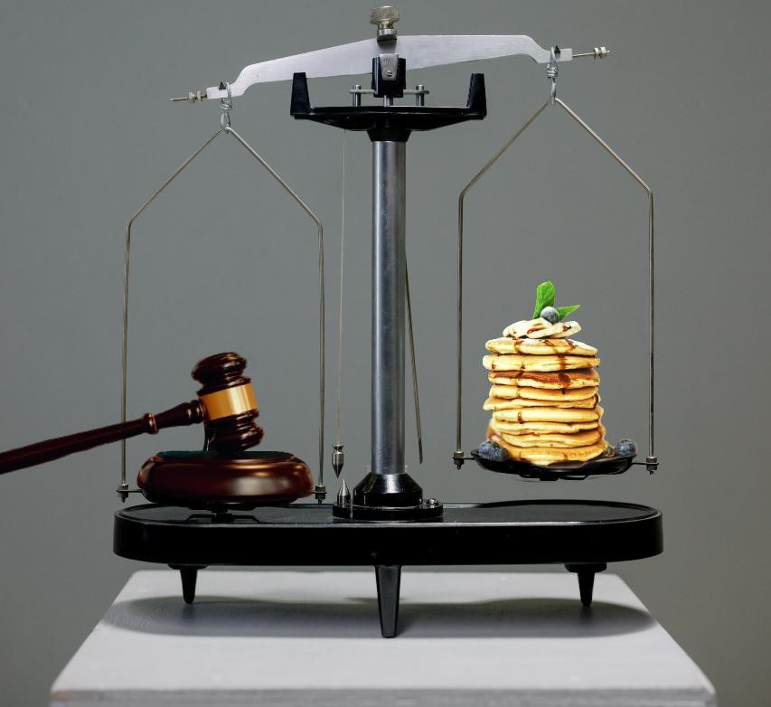 Jessica Dean attorney has balanced trial law with waiting tables over the years. Here is a scale with a judge's gavel on the left which outweighs a stack of syrupy blueberry banana pancakes with a green garnish on top on the right hand side.
